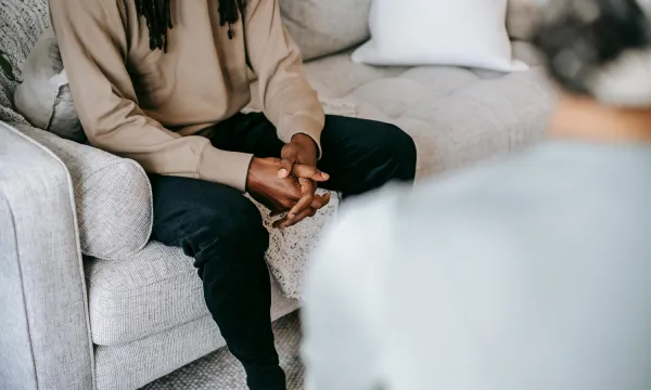 Close-up of a person sitting on a couch, hands clasped during a therapy session